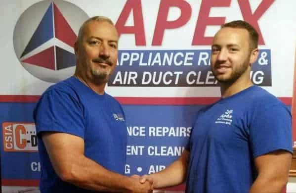 Two men in blue shirts shake hands and smile in front of a sign that reads "APEX Appliance Repair & Air Duct Cleaning," highlighting their expertise in air duct cleaning New Jersey. The logo and additional text appear in the background.