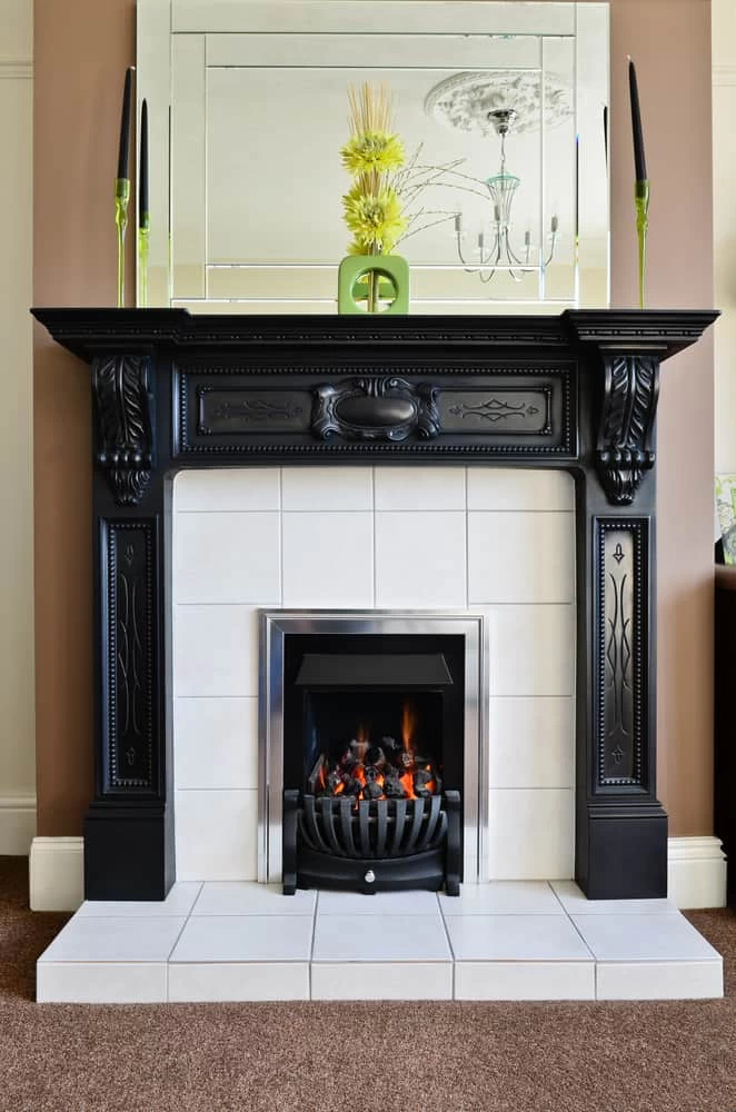 A decorative black fireplace with ornate details surrounds a modern electric fire. The mantel displays two green vases with tall black candles and a yellow floral arrangement—all reflecting a fresh, clean space after air duct cleaning New Jersey.