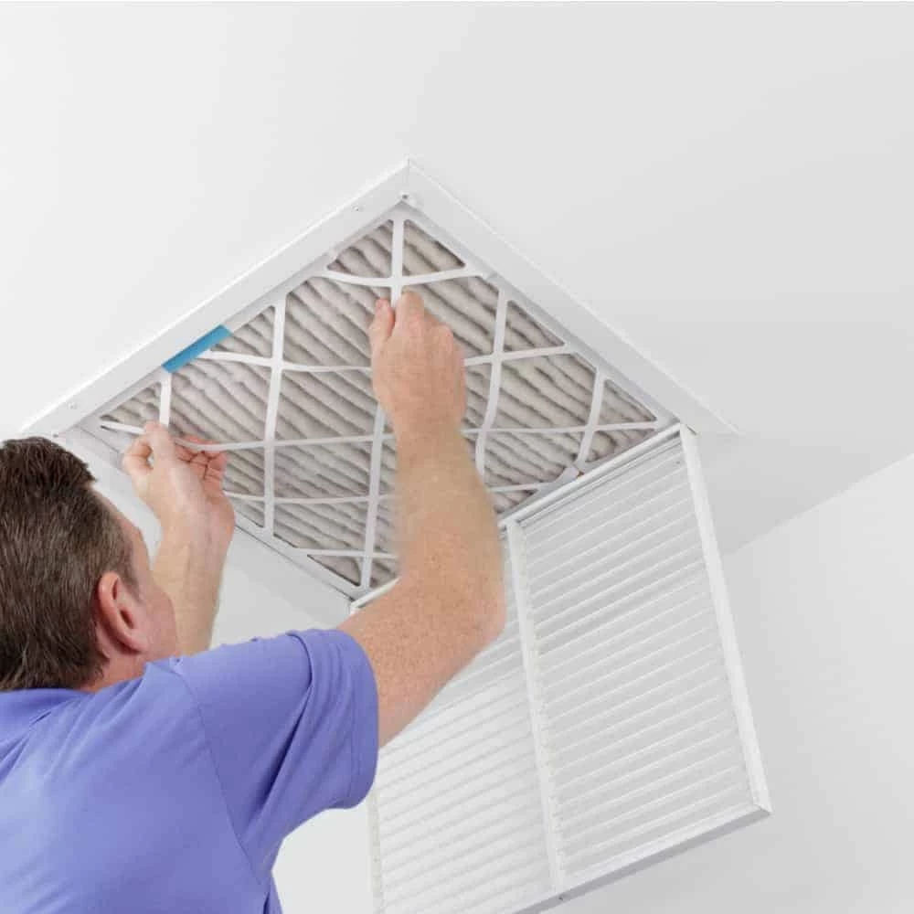 A person in a blue shirt is removing or installing an air filter in a ceiling vent, with the vent cover open—demonstrating professional air duct services New Jersey residents can rely on.