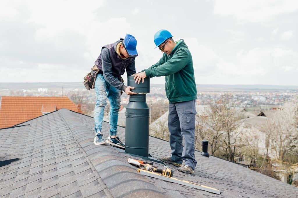 two chimney installers on a house roof.