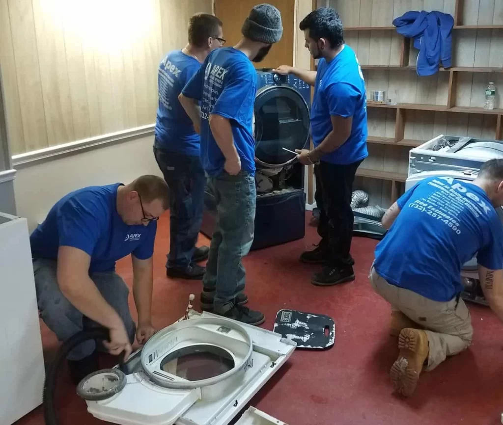 A group of men in blue shirts working on a washing machine.