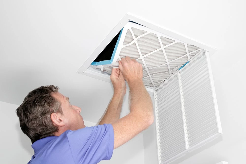 A man is installing a air filter in a ceiling.