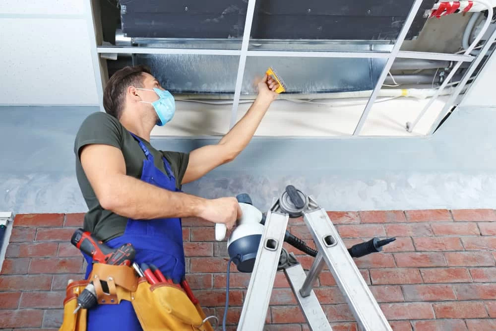 A man is installing a air filter in a ceiling.