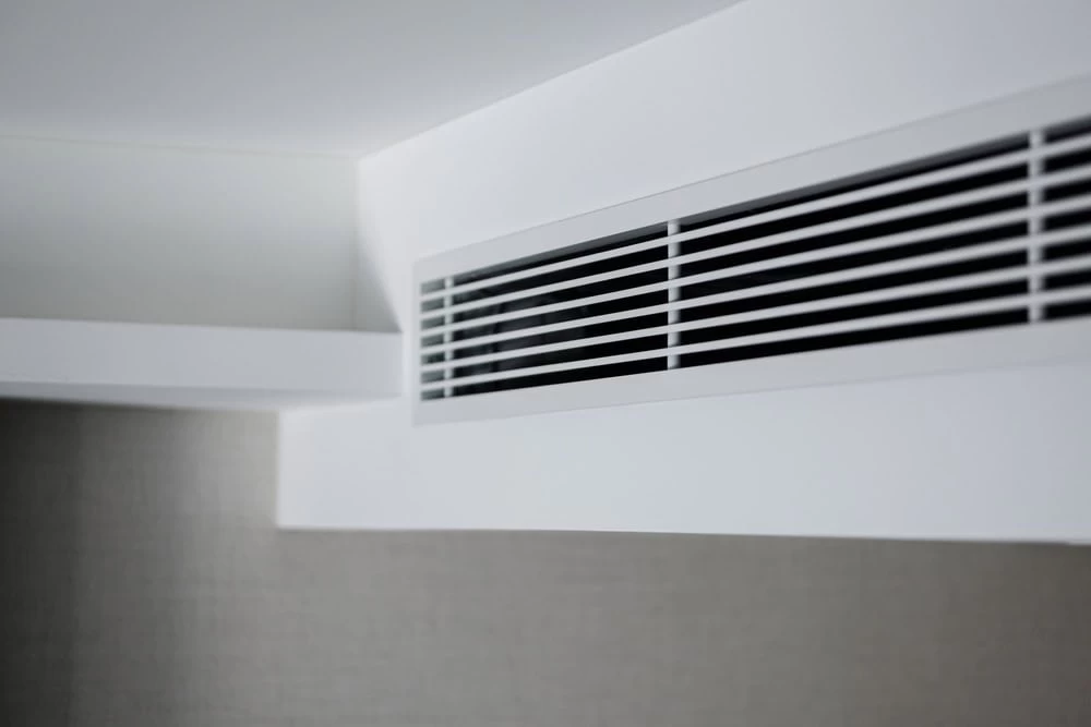 A white air vent in a room with a window.