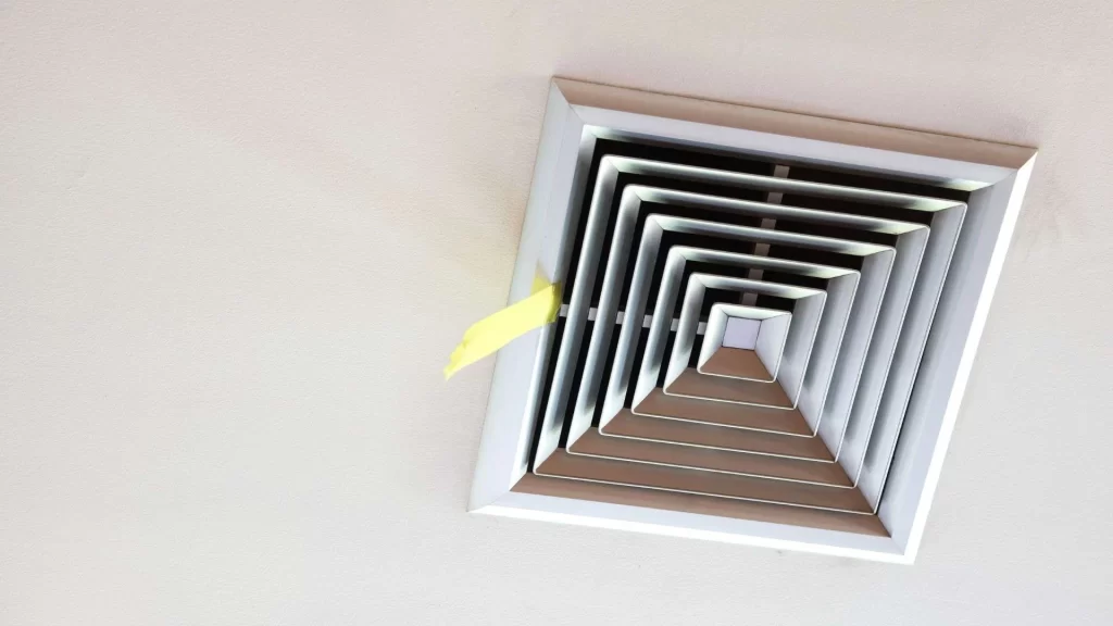 A white ceiling vent with a yellow sticky note.