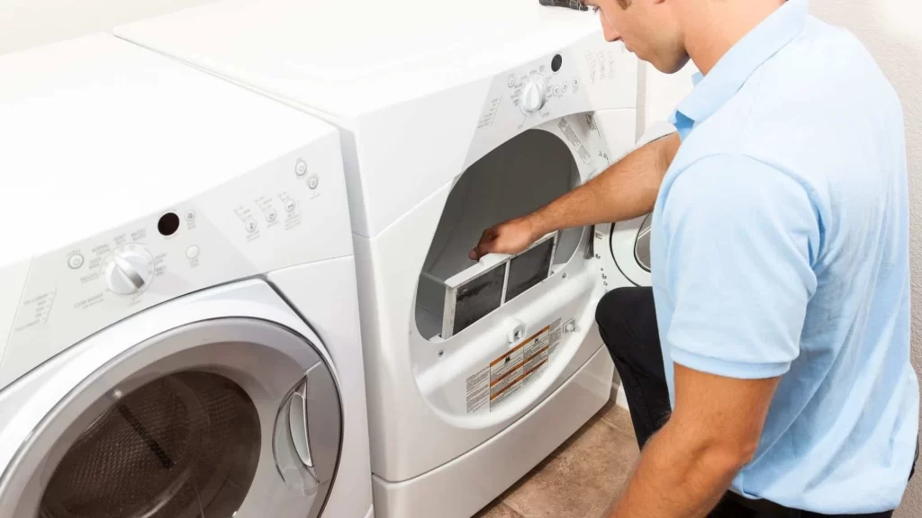 A man is fixing a washing machine in front of a washer.