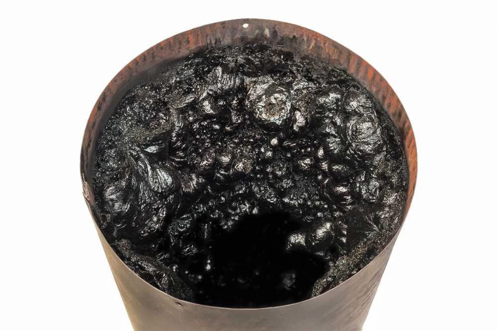 A close-up view of a rusty, cylindrical metal container filled with thick, black, tar-like substance, seen from above against a white background—reminiscent of residue often found during air duct services New Jersey.