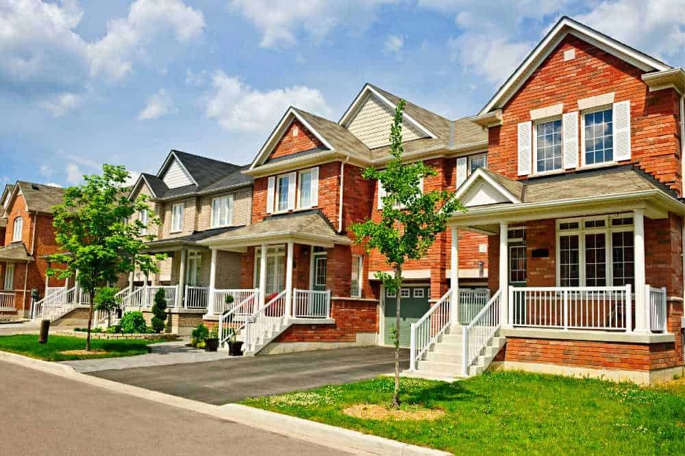 A row of modern, red-brick suburban houses with front porches, green lawns, small trees, and driveways on a sunny day—perfect for families seeking professional air duct services New Jersey trusts.