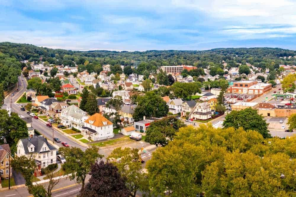 Aerial view of a suburban neighborhood with tree-lined streets, residential houses, and a few commercial buildings surrounded by greenery under a partly cloudy sky—perfect for air duct services New Jersey relies on.